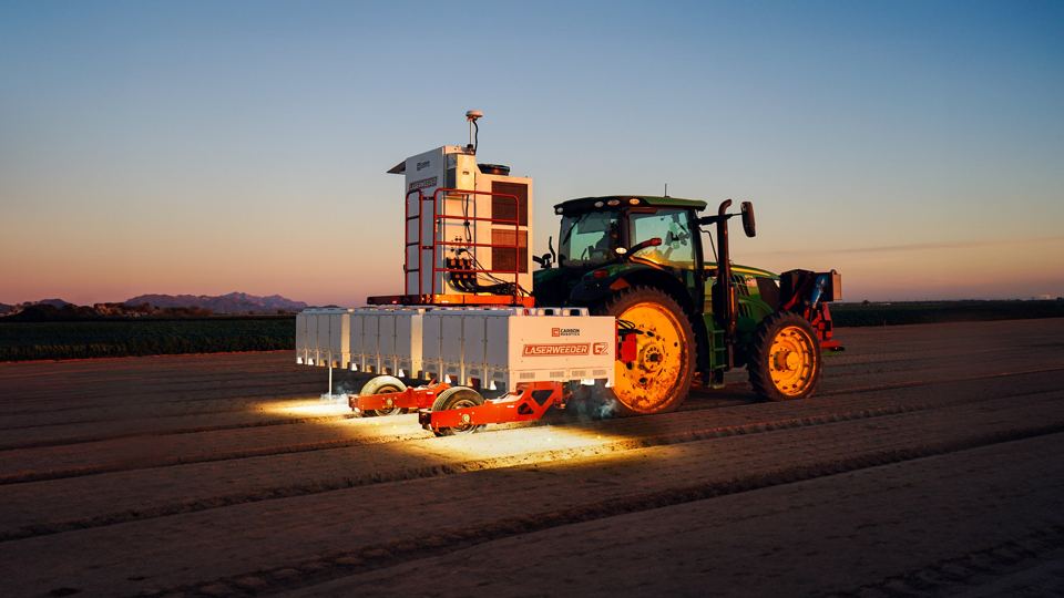 A tractor operates a LaserWeeder G2 600 at dusk.