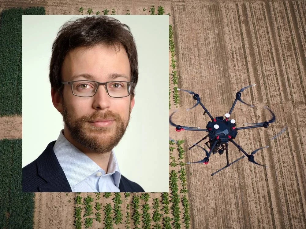 Portrait of Stefano Mintchev with a research drone and agricultural plots in the background.