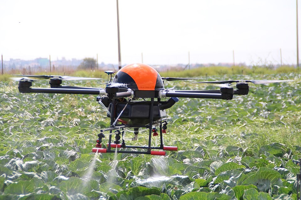 An agricultural multirotor drone applies spray over a leafy crop.