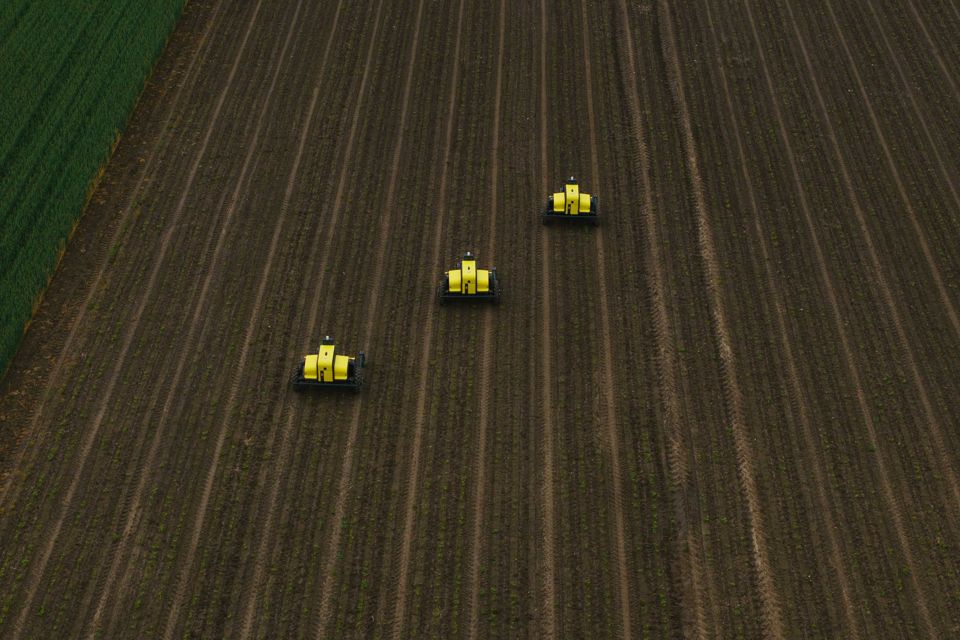 Three yellow Kilter AX-1 robots work across a field.