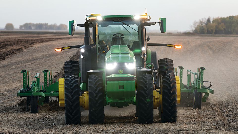 John Deere 8R tractor working with a tillage implement in a field.