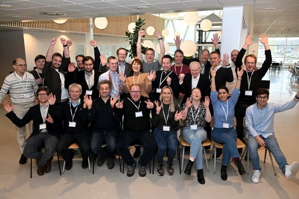 A group of seminar participants posing indoors and raising their hands.