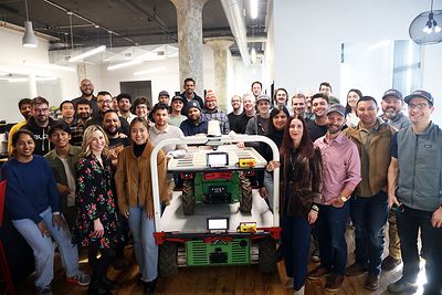 The Burro team stands with a Burro Grande robot inside a facility.
