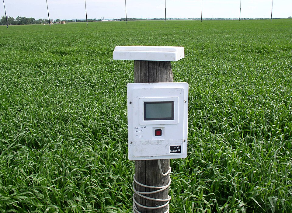 A soil-moisture data logger mounted on a wooden post beside an irrigated field